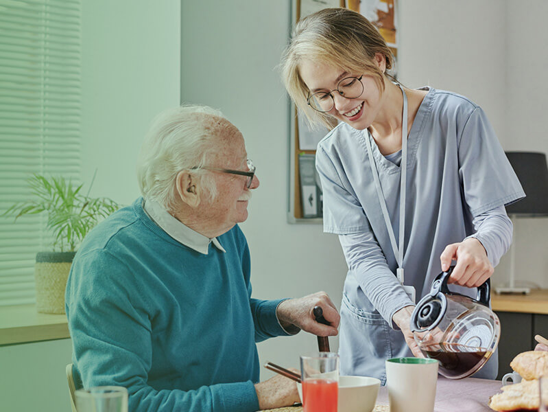 Young female nurse pouring an older man coffee