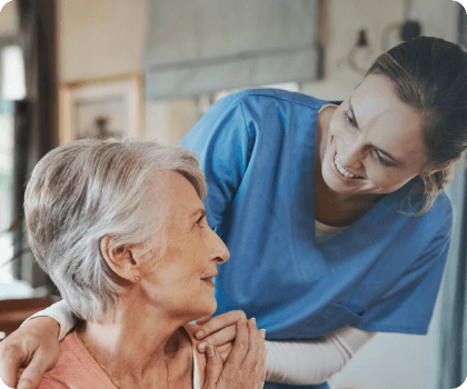 Nurse looking down at elderly woman, smiling at her, and grabbing her shoulder.